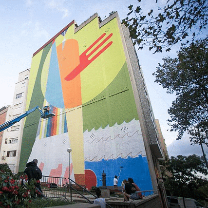 Artistas anónimos de pie frente a un vibrante mural de grafiti urbano con un ascensor utilizado para pintar