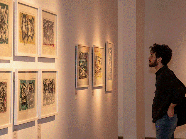 Una persona observa atentamente obras de arte abstractas enmarcadas en un entorno de galería íntimo, ilustrando tesoros artísticos ocultos.