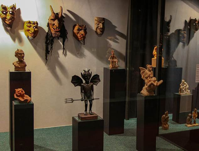 Una exhibición de museo con esculturas y máscaras demoníacas inusuales que muestran arte alternativo y macabro.